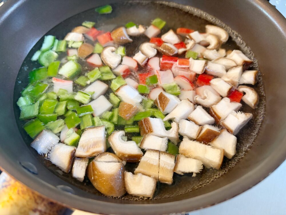 チャーハンを盛りつけたら、今度は餡を作る。フライパンに水とガラスープ、にんにくと生姜を入れ、具も加えて煮立てる。具に火が通ったら片栗粉でとろみをつける。