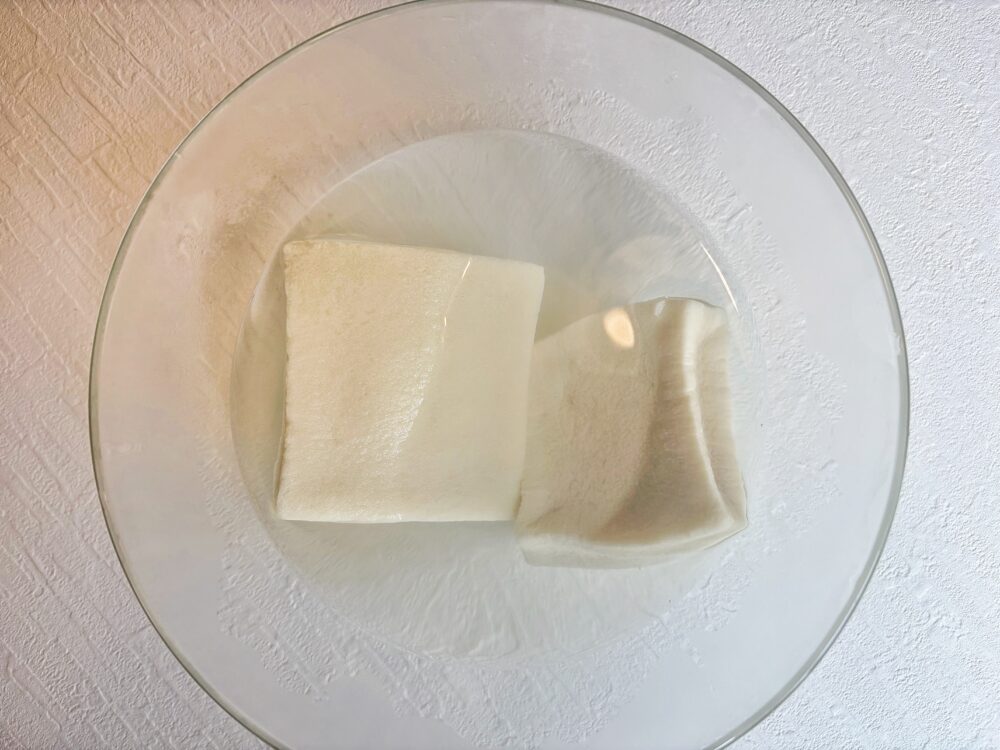 高野豆腐をお湯で戻す。ふっくら倍くらいの大きさに戻ったら、よく押し洗いをして手で挟んで水気を絞り、半分に切っておく。