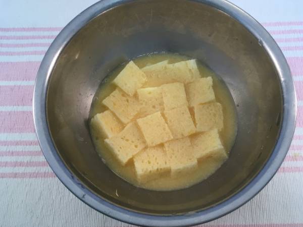 ボールに卵を入れ、かきほぐし、分量のりんごジュースを加えて、さらによくかき混ぜる。そのなかに16カットにした食パンを入れ、浸す。