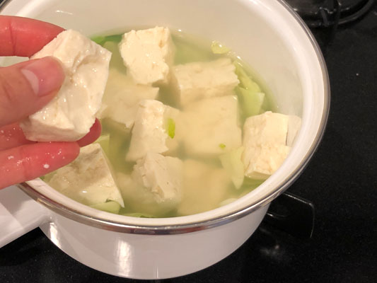 1のスープが沸騰したら、キャベツと小松菜の茎、豆腐を手で崩しながら加える。